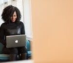 African American woman happily working on a laptop in a modern office setting.